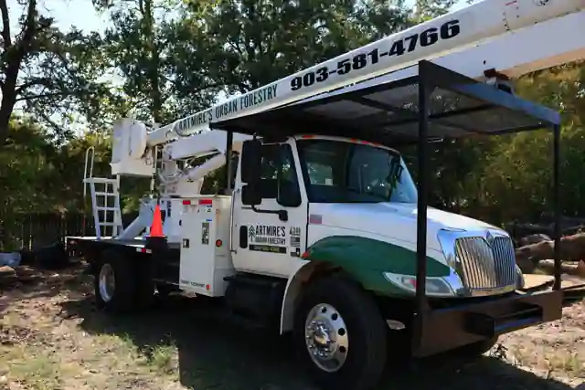 The Artmire's white and green International bucket truck in the yard, the company name and office number lettered on the boom and door