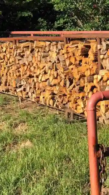 Split firewood stacked in a long rack with red rails