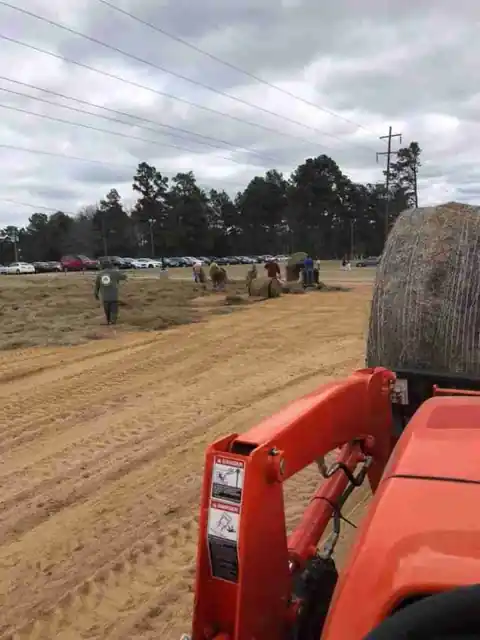 An orange tractor with a straw bale on a graded field while a crew spreads straw