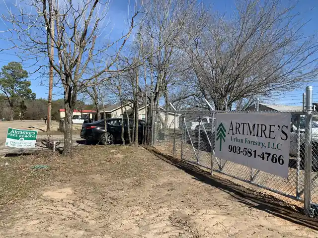 The Artmire's chain-link yard on Bellwood Golf Club Rd with the banner Artmire's Urban Forestry, LLC and the office number, bare winter trees behind